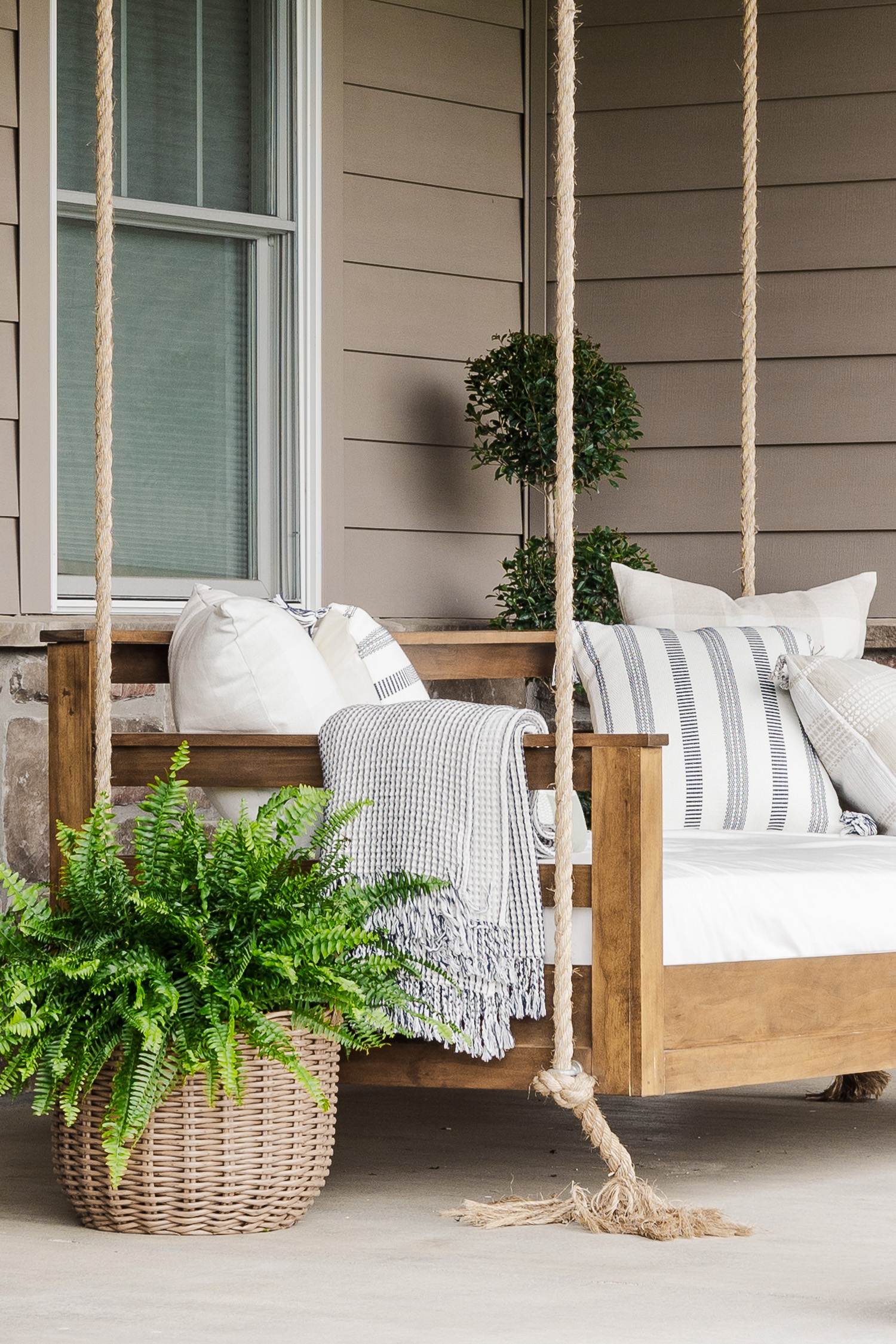 wood patio swing with green plants and pillows and blanket