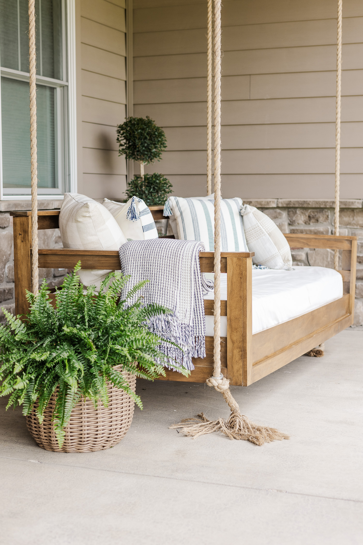wood patio swing with green plants and pillows and blanket