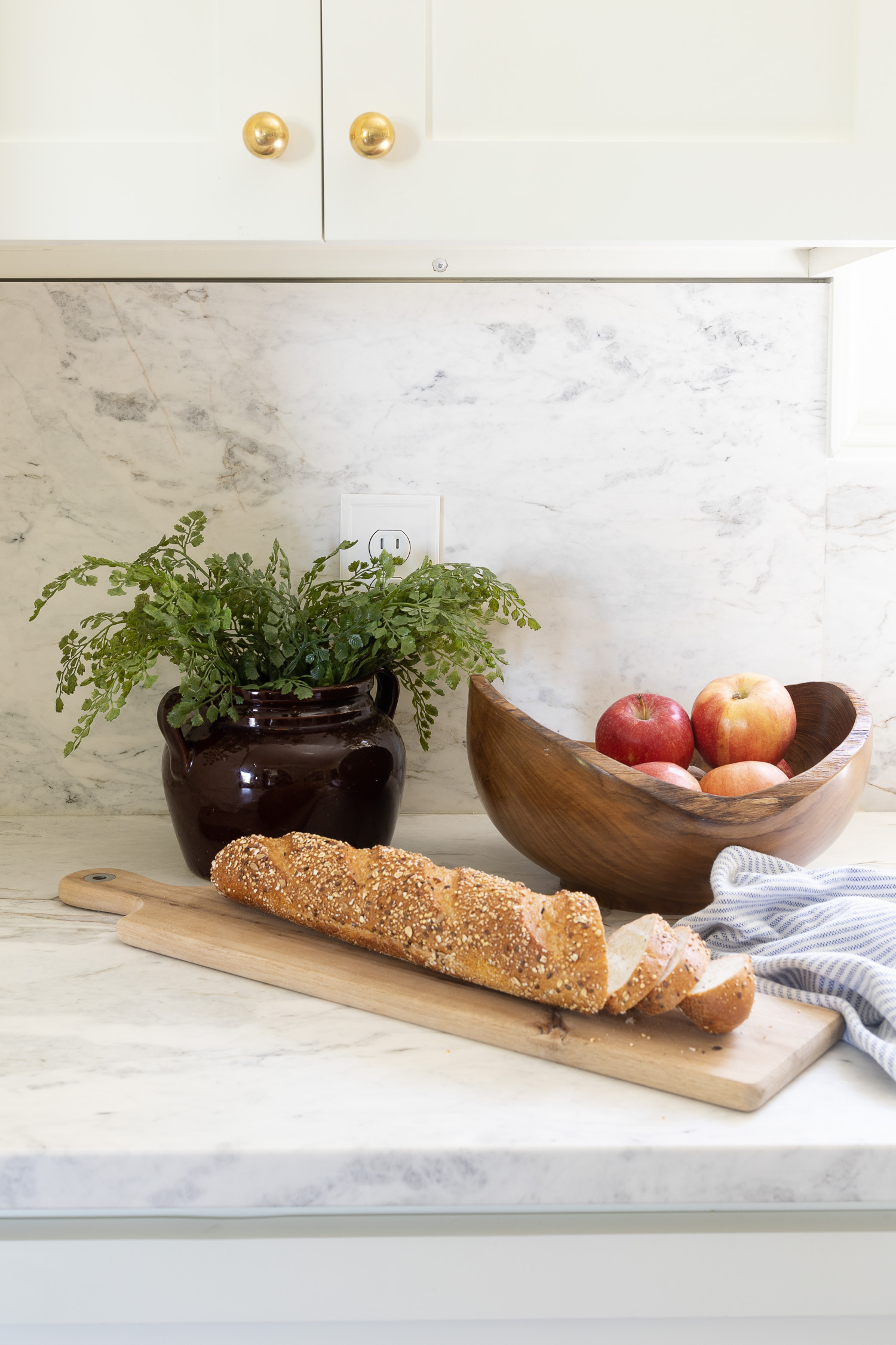 white kitchen cabinet and marble kitchen countertop with bowl of apples and bread on board