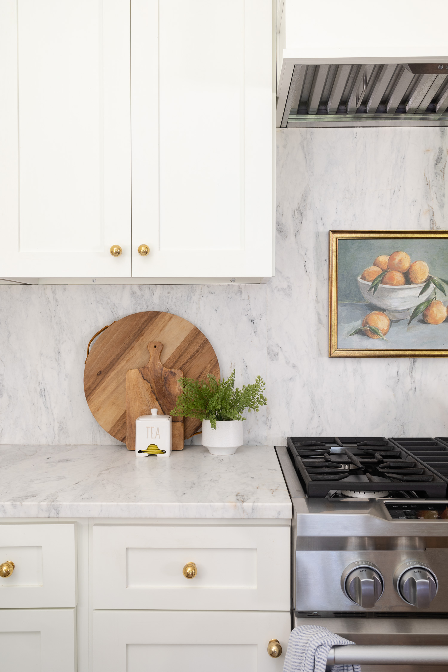 white and kitchen with marble backsplash and fruit art print above gas range