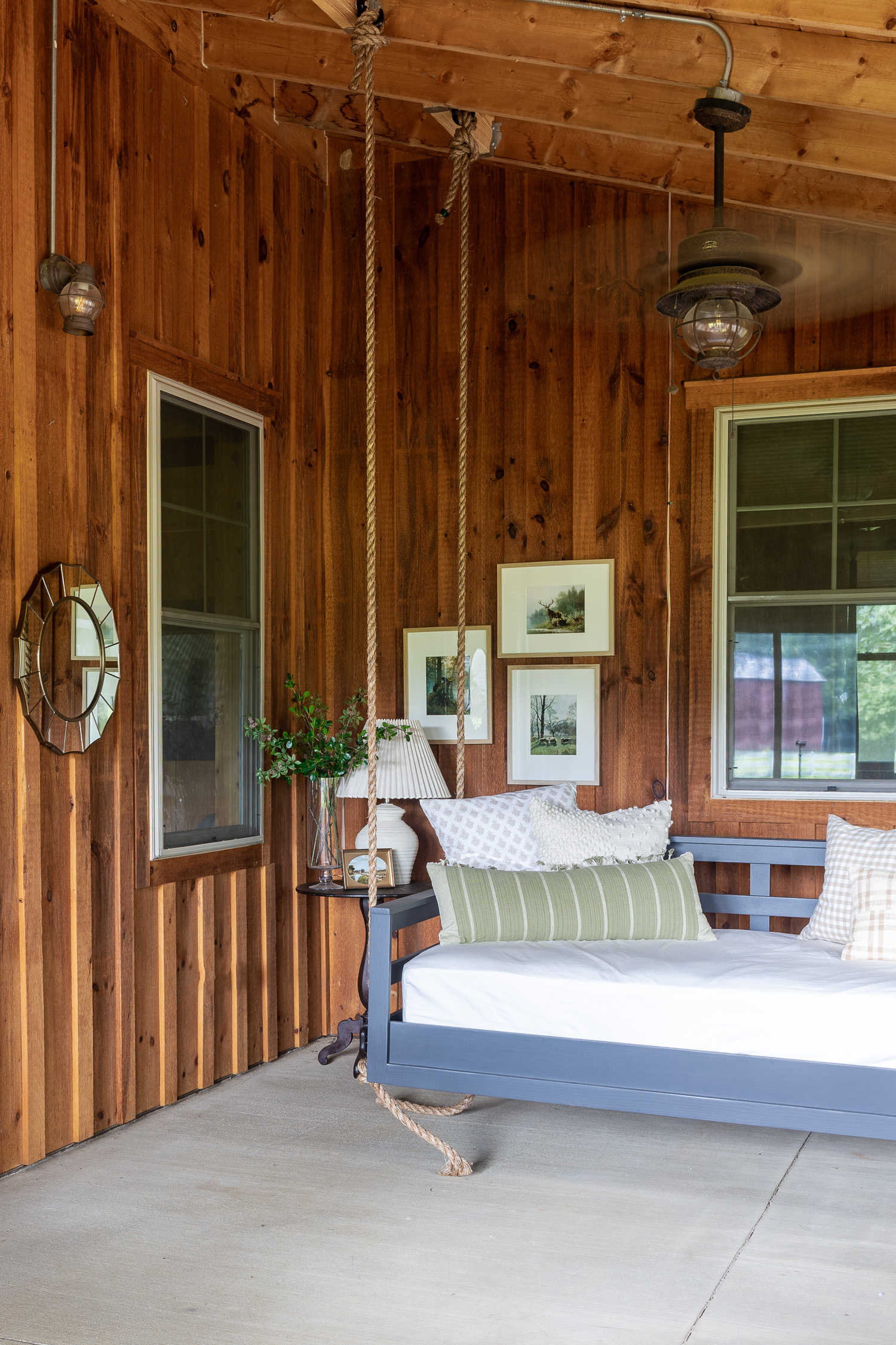 barndominium screened in porch with bed swing, artwork, lamp and pillows