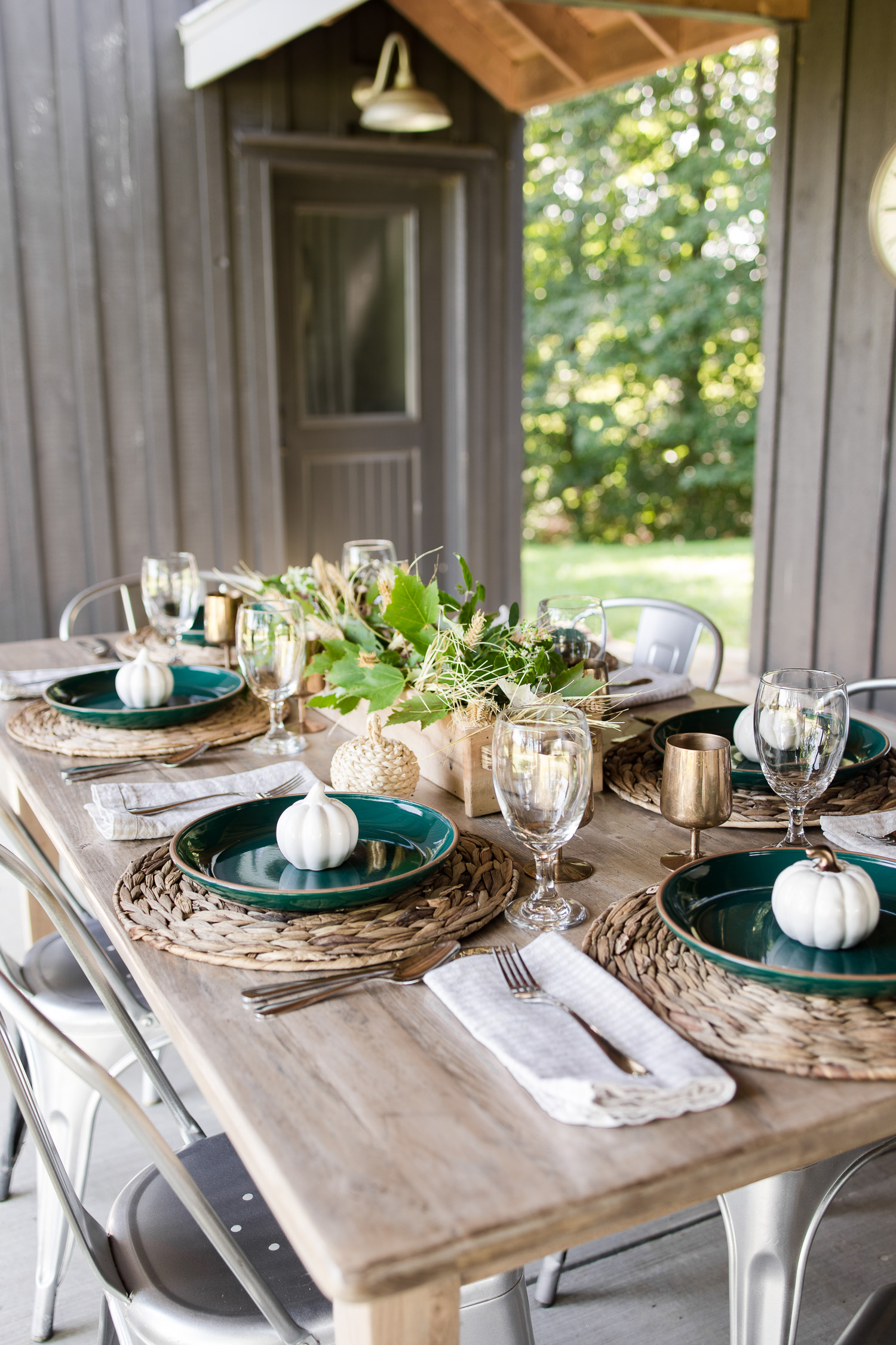 fall tablescape on the outdoor back patio with green plates, wooden table, silver metal chairs, pumpkins and brass goblets