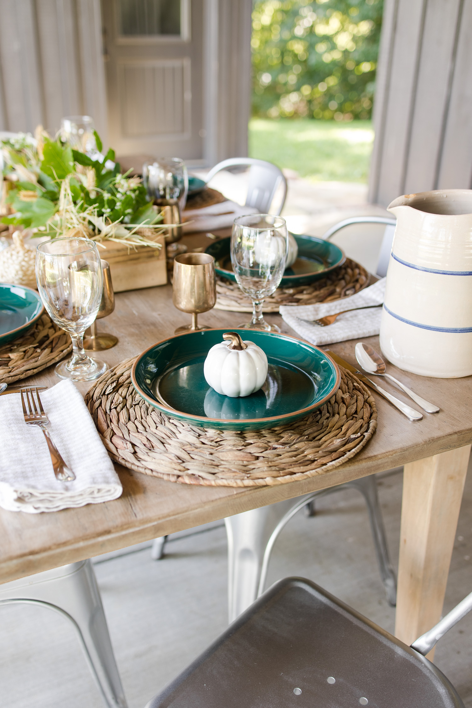 fall tablescape on the outdoor back patio with green plates, wooden table, silver metal chairs, pumpkins and brass goblets