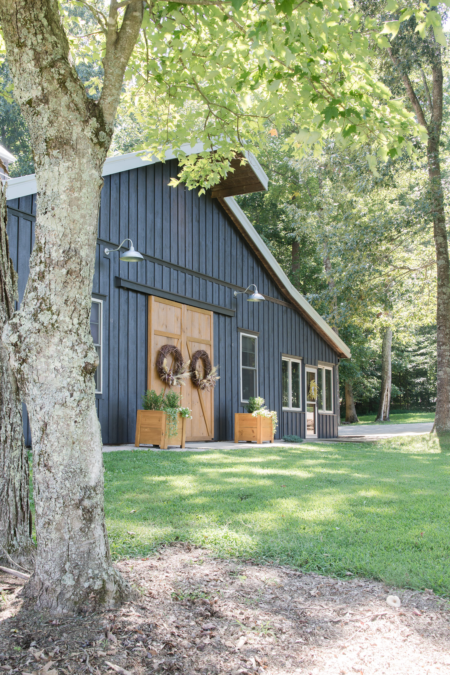 black barndominium with wood board and batten. Wood barn doors, with large wreaths, planters and galvanized barn lights
