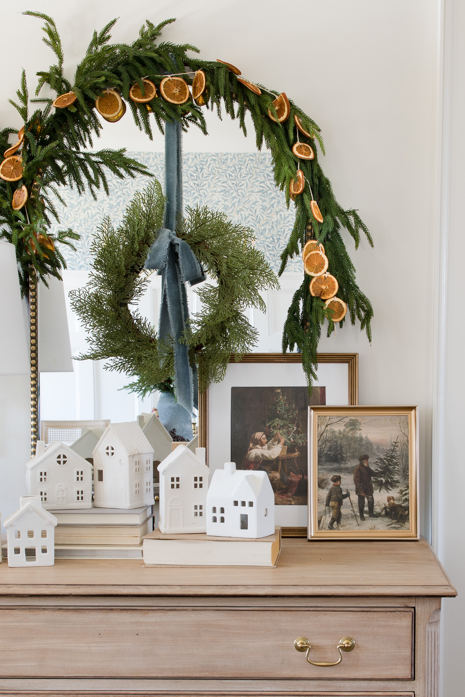 white christmas village on dresser with pine garland and christmas vintage prints framed