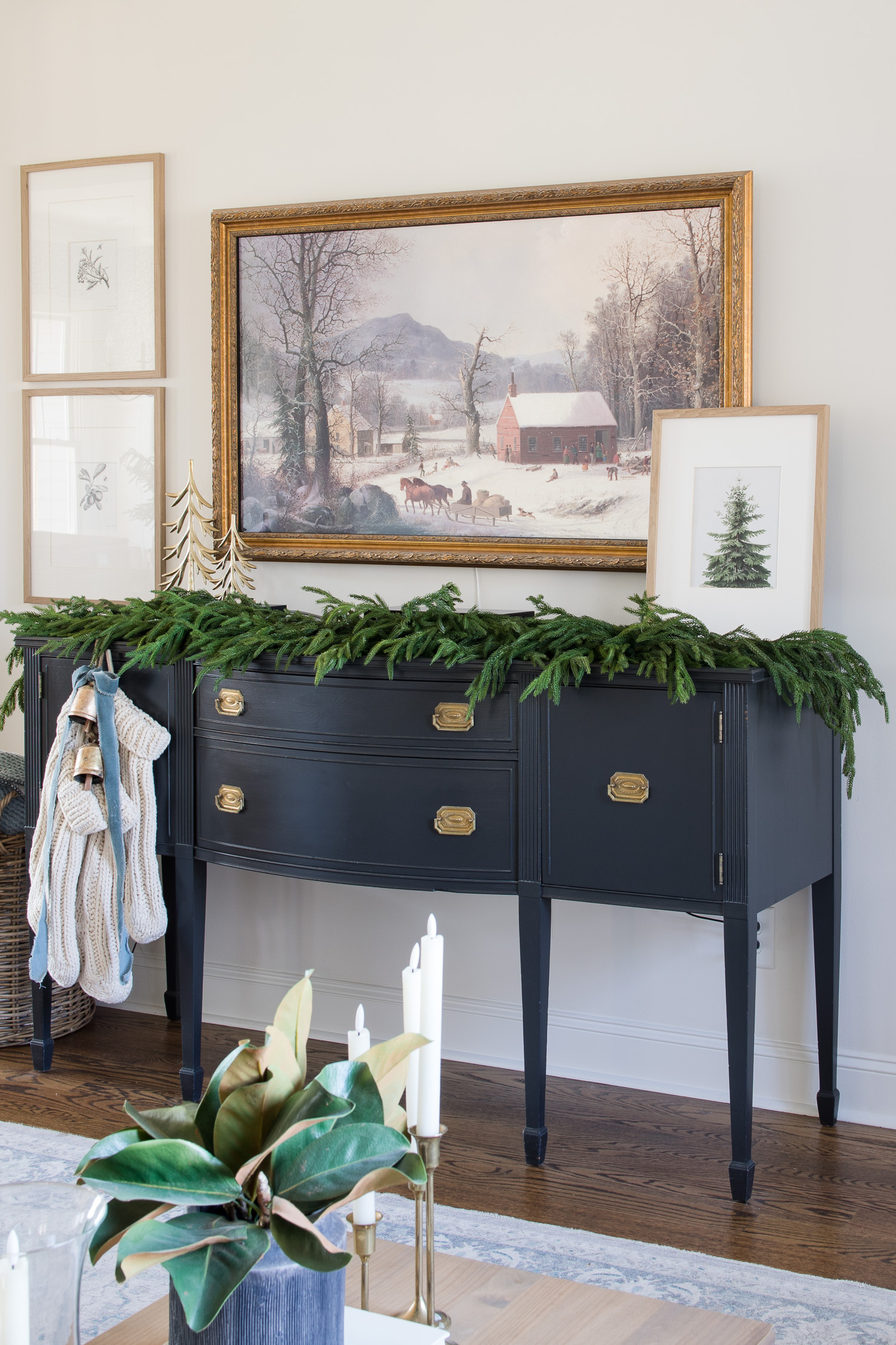 black buffet with pine garland and stockings with framed winter tv art