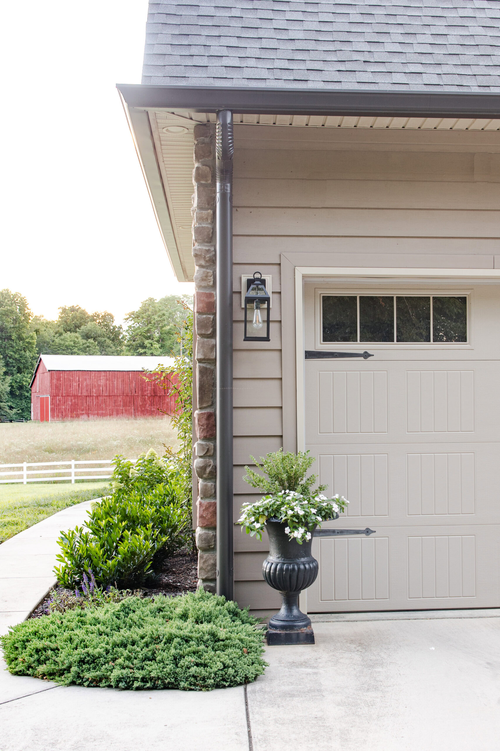 outdoor light next to garage with outdoor planter with boxwood and white florals next to sidewalk