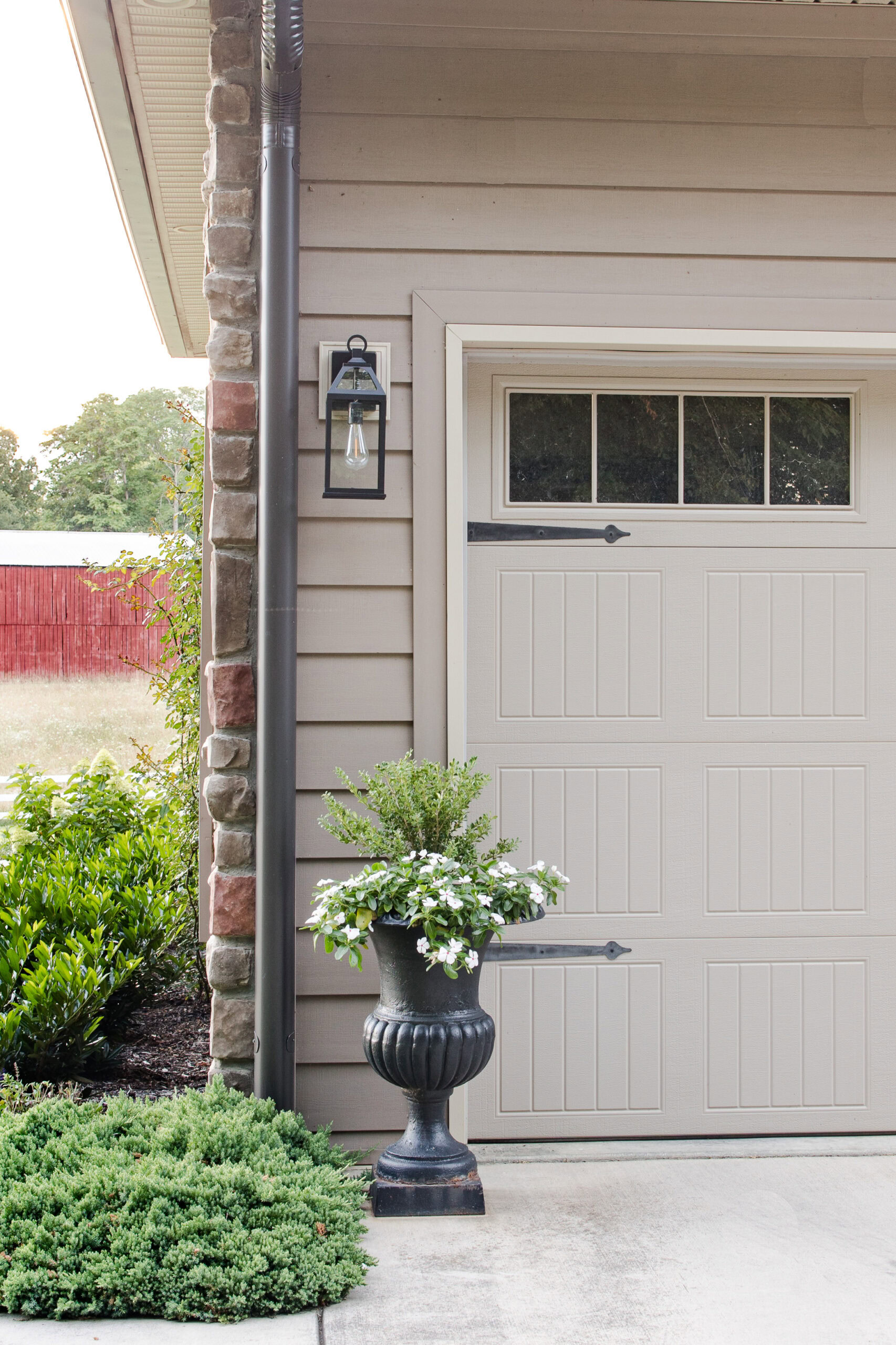 outdoor light next to garage with outdoor planter with boxwood and white florals next to sidewalk