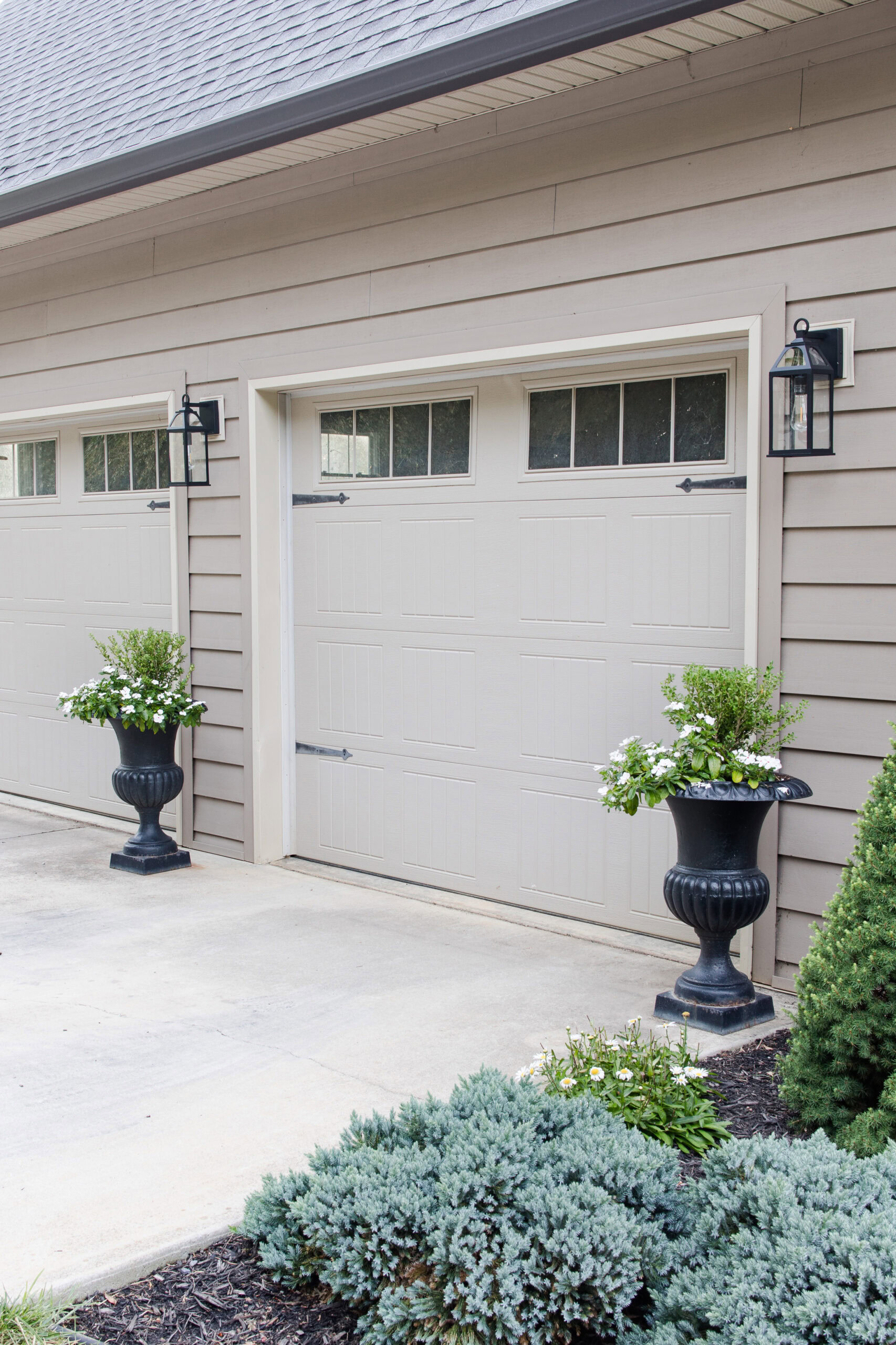 outdoor light next to garage with outdoor planter with boxwood and white florals next to sidewalk